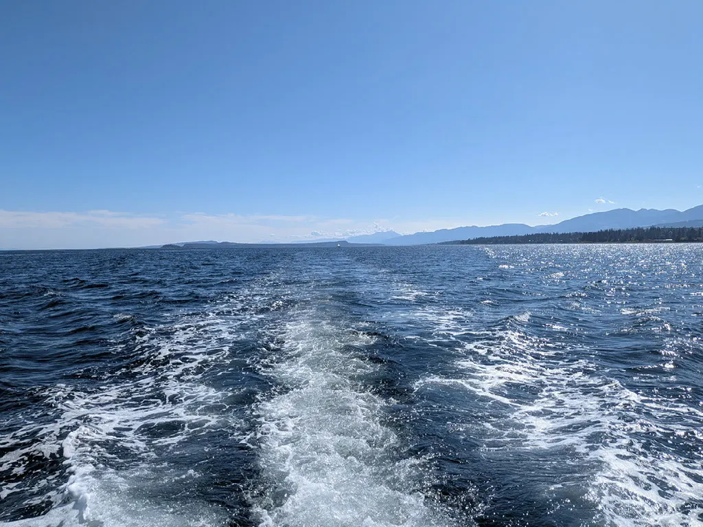 Boat wake crossing open water toward Vancouver Island mountains